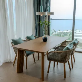 Wood dining table surrounded by woven rattan chairs beside a large window