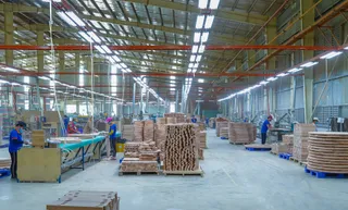 Wide furniture factory floor with production lines, workers and stacked wooden components
