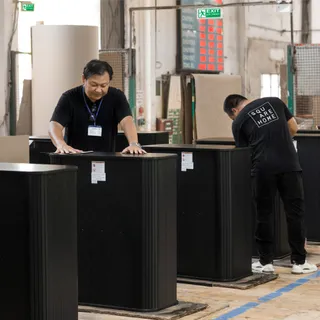 Workers inspecting black furniture cabinets on a factory floor