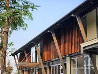 Timber-clad building exterior with angled supports, balcony and glass doors.