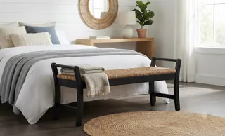 Woven bench with dark wooden frame at the foot of a bed