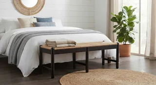 Dark wooden bench with woven seat at the foot of a bed