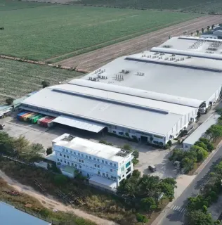 Aerial view of a large white-roofed furniture manufacturing facility beside fields and a road.