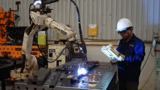 Worker using robotic welding equipment at a metal fabrication table