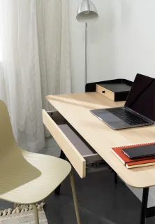 Light wood office desk with integrated drawer beside a curved chair