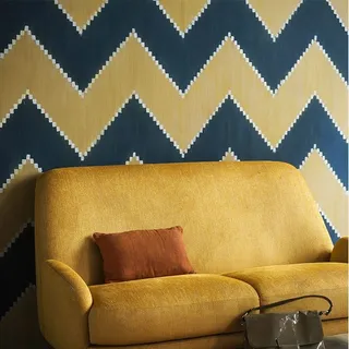 Mustard yellow upholstered sofa with cushions against a geometric wall