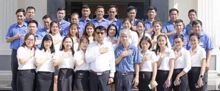 Large group of factory employees posing together outside a building