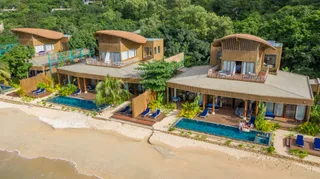 Aerial view of timber villas with pools and decks along a beach