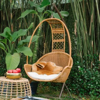 Hanging woven rattan chair and matching table in a leafy garden