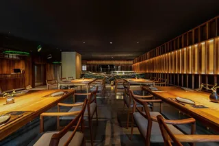 Dark wood restaurant interior with dining tables, chairs and warm lighting.