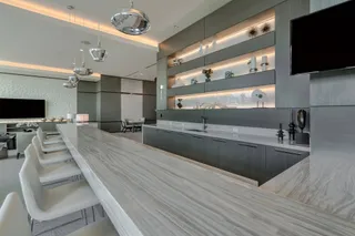 Modern showroom interior with a long marble-look table, white chairs, cabinetry, and display shelving.