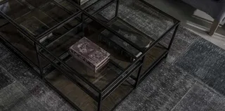 Black metal and glass coffee tables arranged on a textured rug.